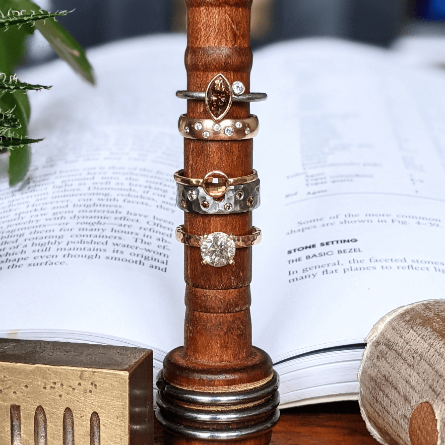 Handmade rings stacked in front of a book on making jewelry.