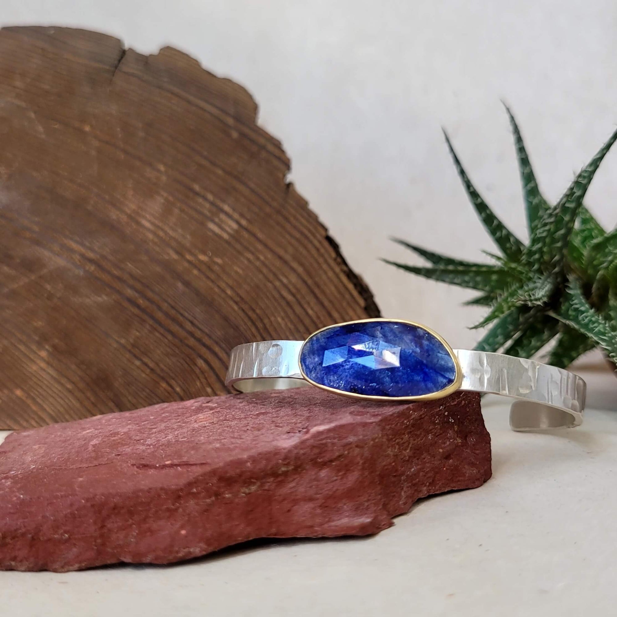 Organic shaped rose cut blue sapphire cuff with a yellow gold bezel on a hand hammered sterling silver cuff.