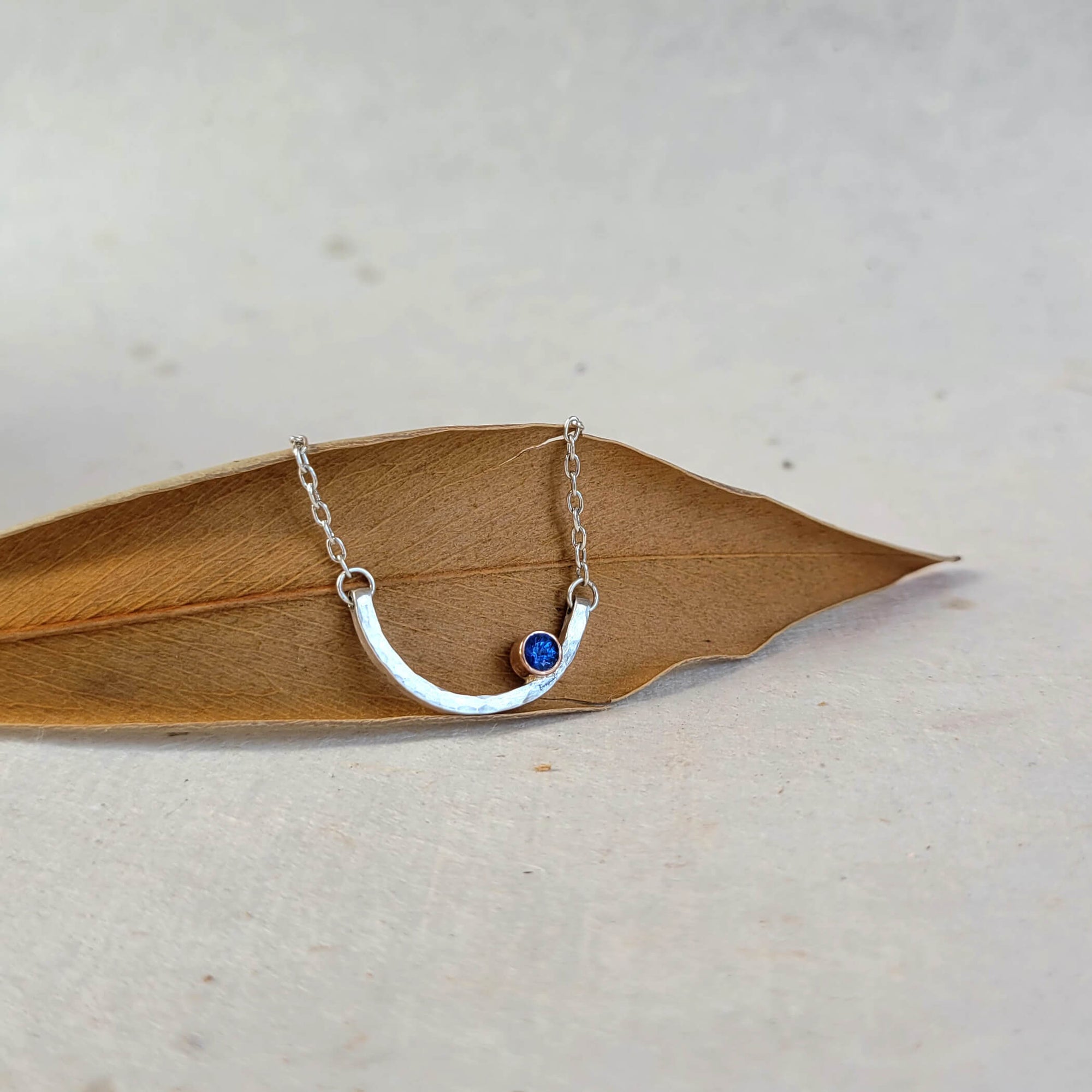 Hammered sterling necklace with blue sapphire accent bezel set in rose gold.