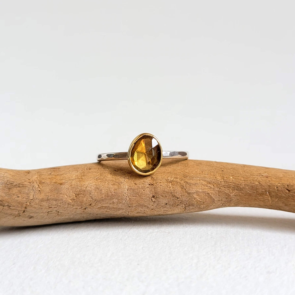 An irregular yellow sapphire ring with a bezel setting, placed on a wooden branch against a white background.