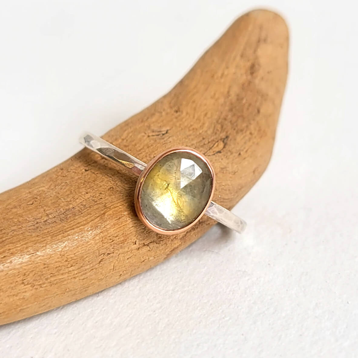 An oval green sapphire ring in a rose gold and silver setting, displayed on a wooden surface.