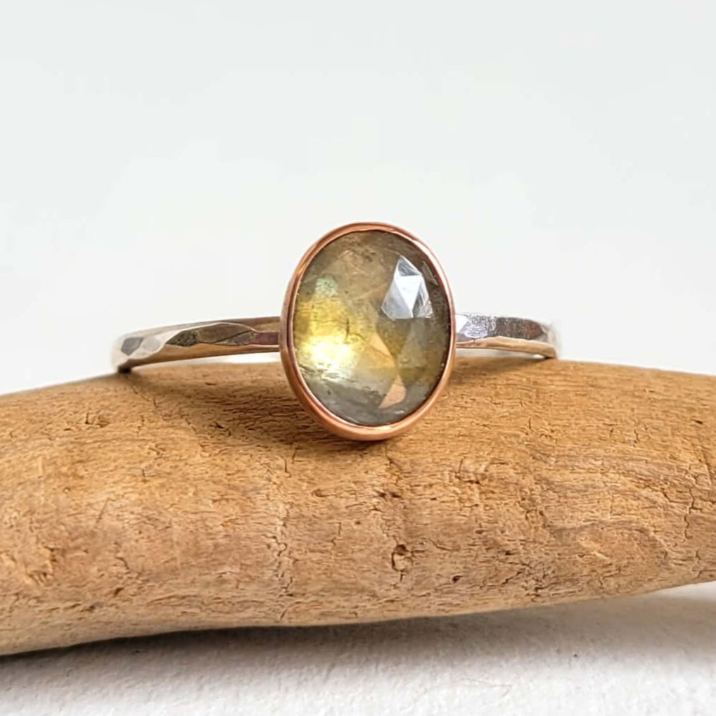 Silver ring with a green gemstone on a piece of driftwood against a white background