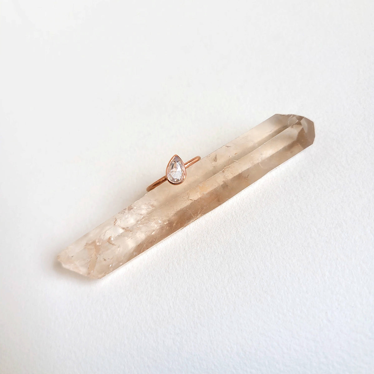 Smoky quartz crystal with a rose gold ring on a light gray background
