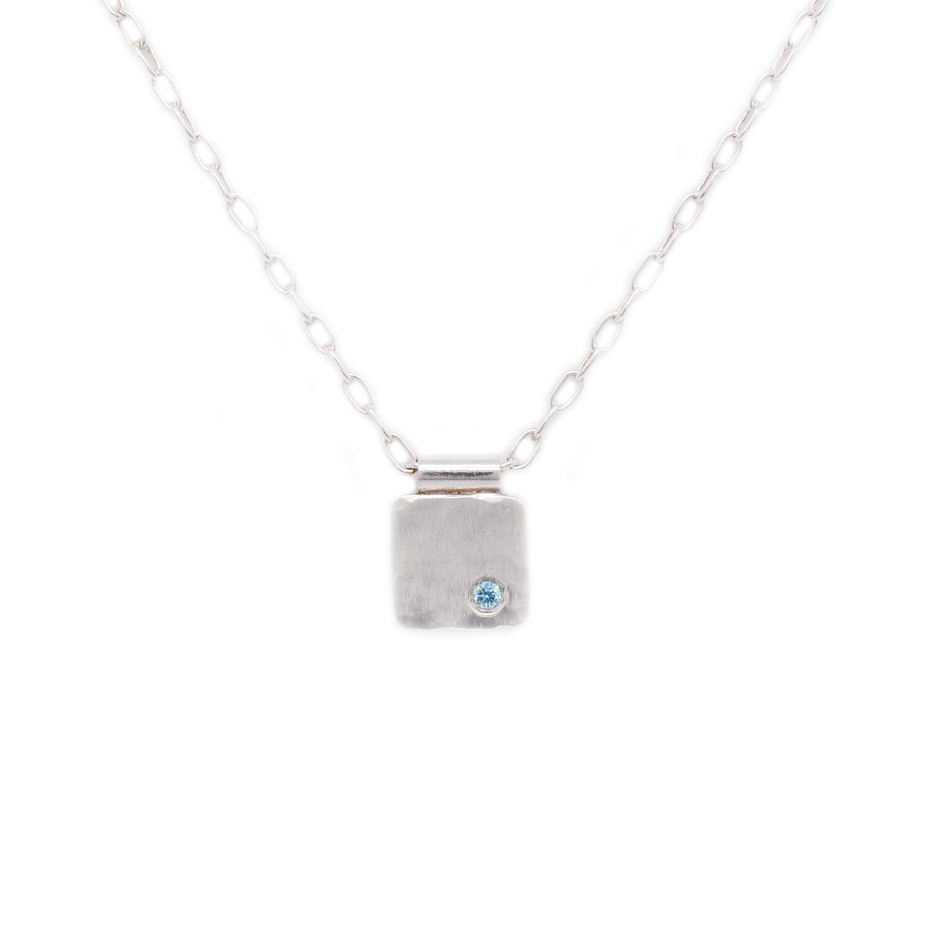 Pendant necklace with flush set teal blue diamond on a hammered silver cell.