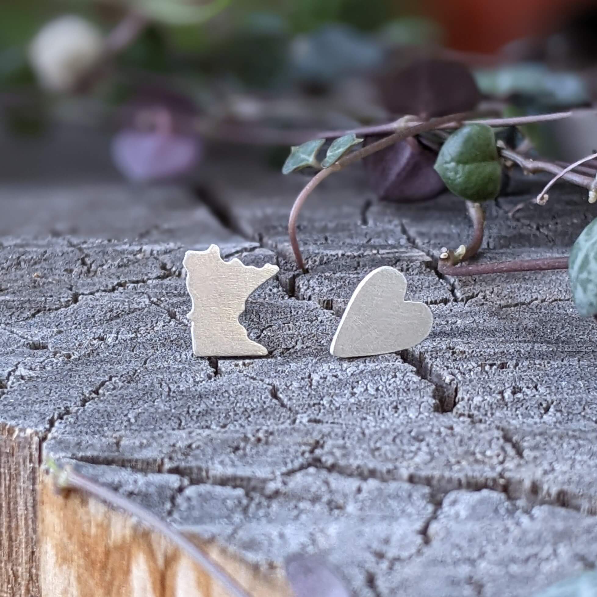 Mis-matched stud earrings in sterling silver. One earring is shaped like the state of Minnesota and the other is shaped like a heart.
