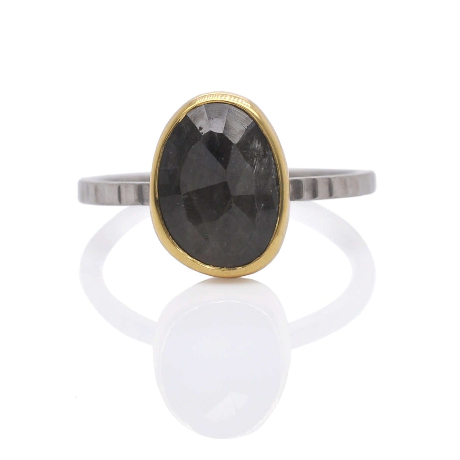 Organic shaped sapphire solitaire with a yellow gold bezel on a linear hammered band of palladium.