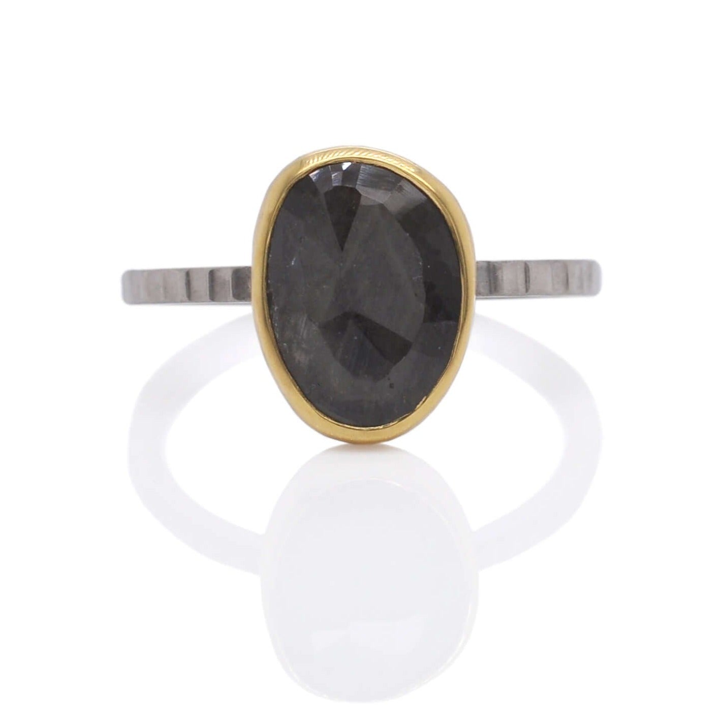 Organic shaped sapphire solitaire with a yellow gold bezel on a linear hammered band of palladium.